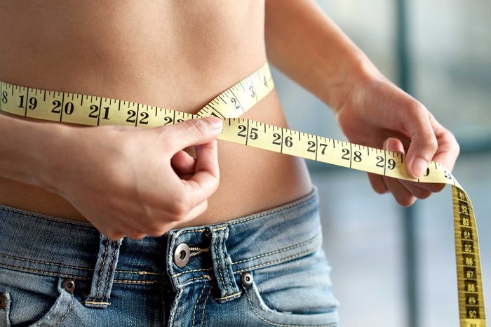 Woman wearing jeans wrapping a tape measure around her waist.
