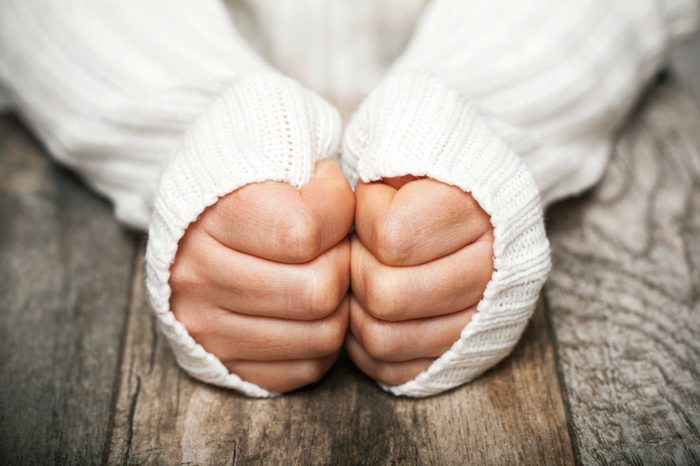 Woman in a white sweater wearing her sleeves high on her hands to keep warm.