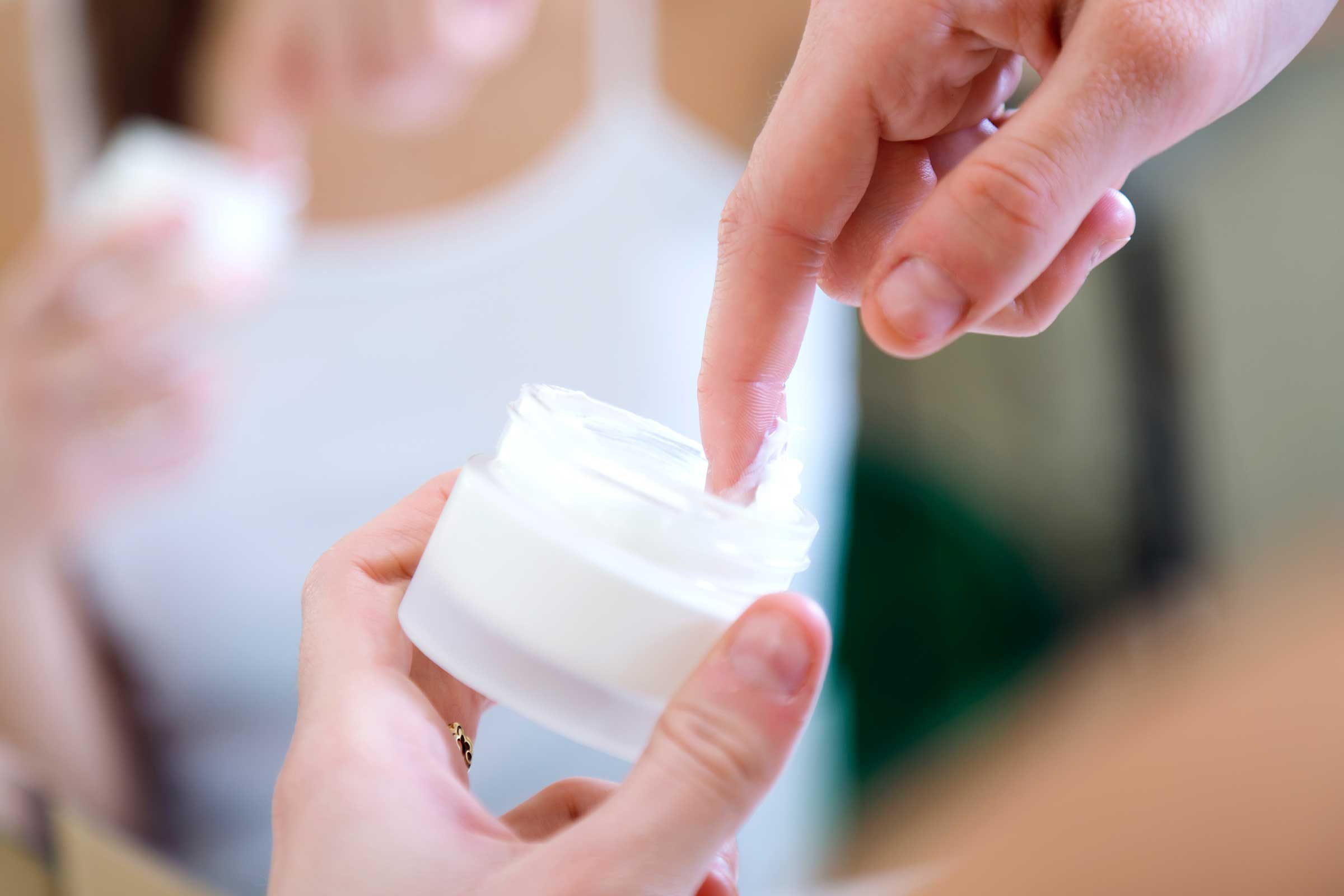 Finger dipping into a jar of cream.