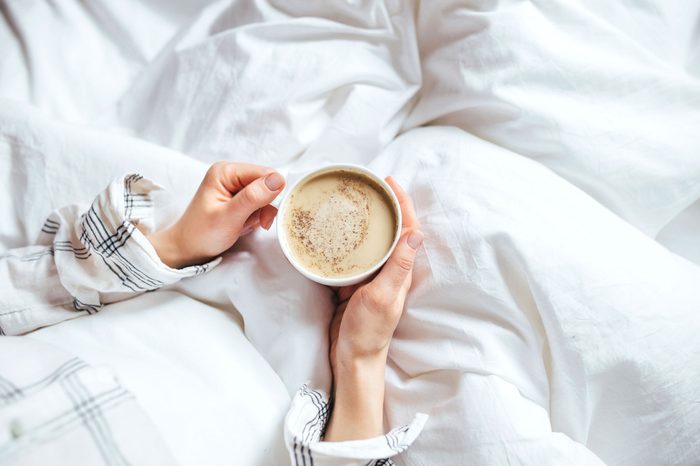a person in bed holds warm drink