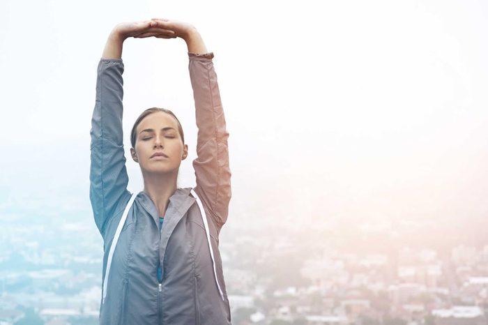Woman in a windbreaker stretching her arms over her head.