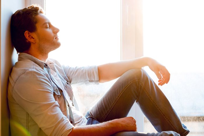 man with eyes closed leaning against wall