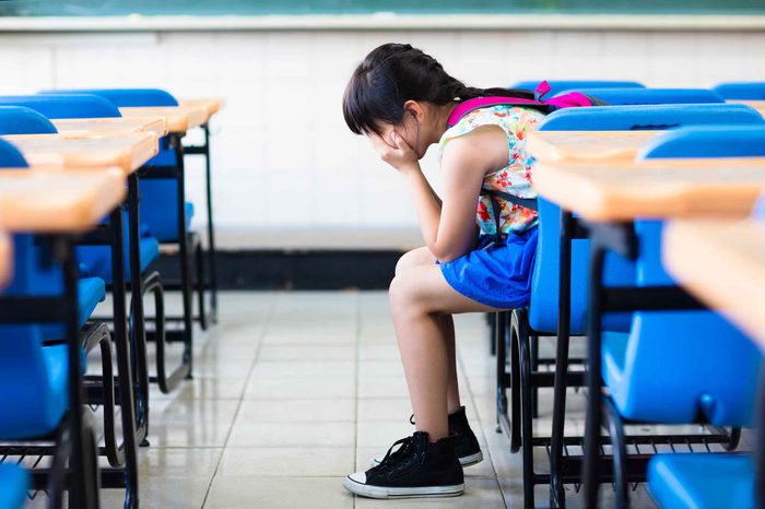 Little kid in a classroom with their hands covering their face.
