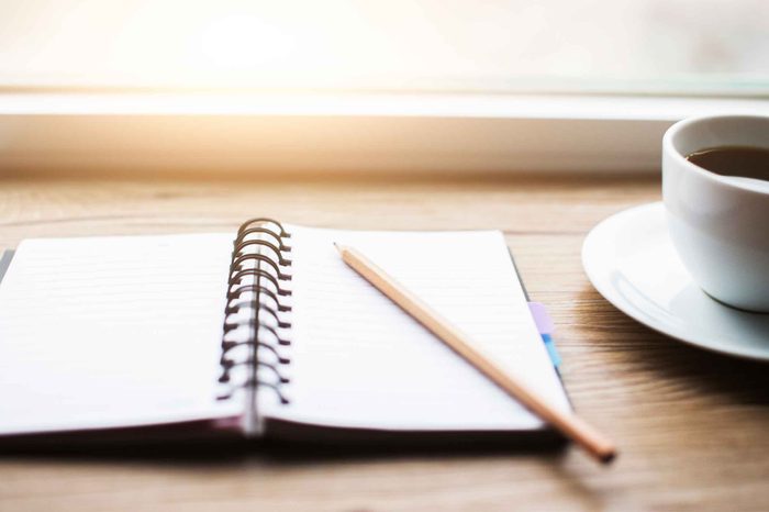 journal with pencil on a table next to a cup of coffee