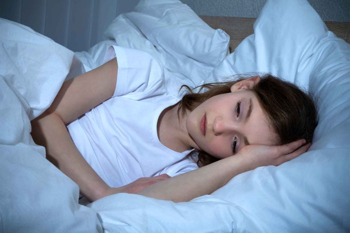 Little girl lying in white bed trying to sleep.