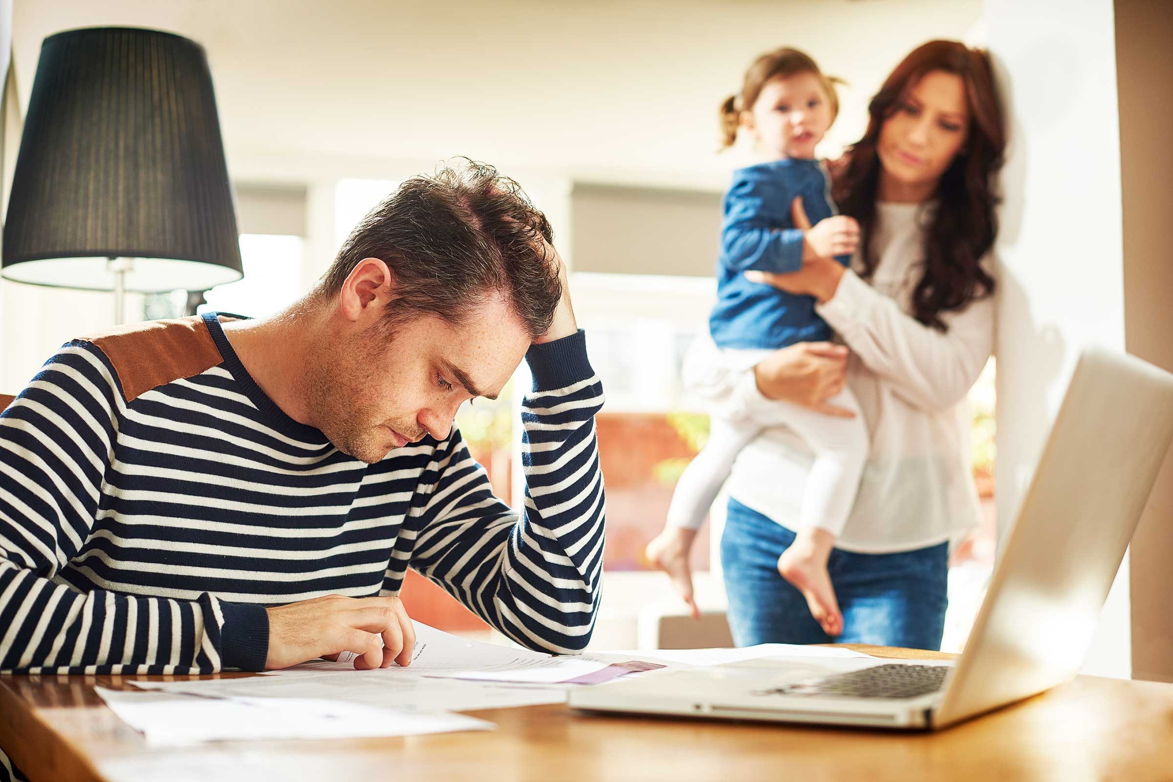 Man at his desk at home looking stressed as he reviews paperwork.