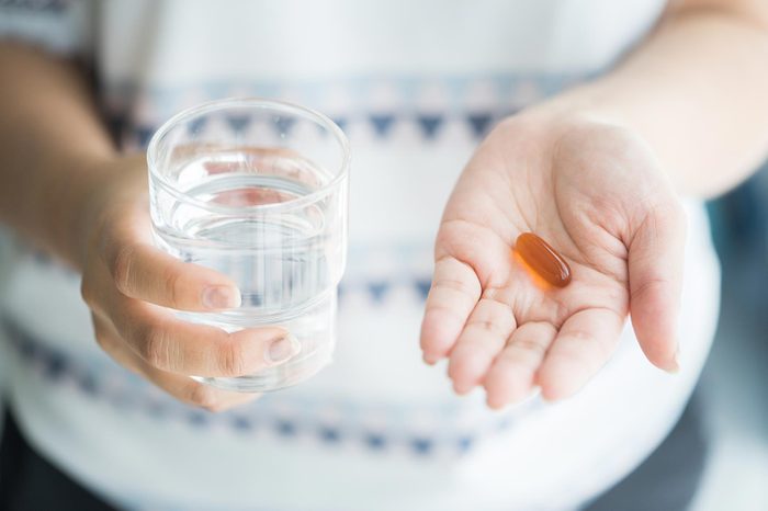 woman with of glass of water in one hand and capsule in the other
