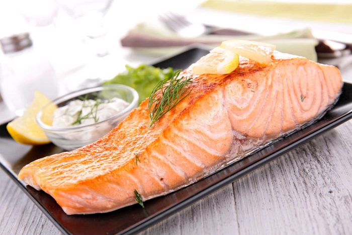 cooked salmon filet on a plate with dill sauce and lemon wedge