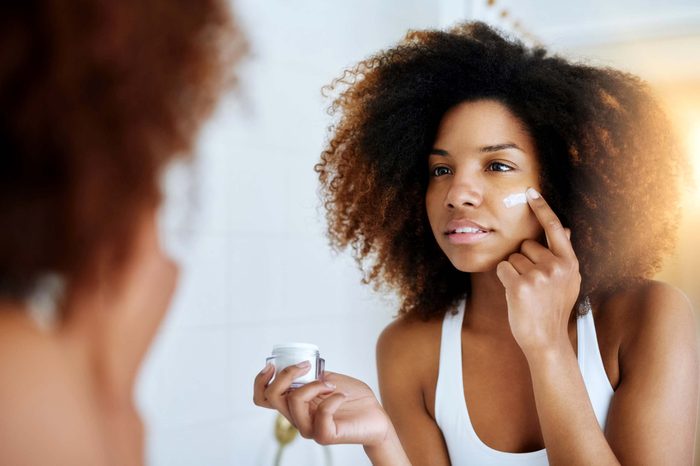lovely young woman looking in mirror and putting on face cream