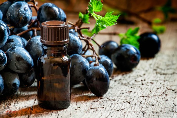 brown vial on wood table with grapes behind it