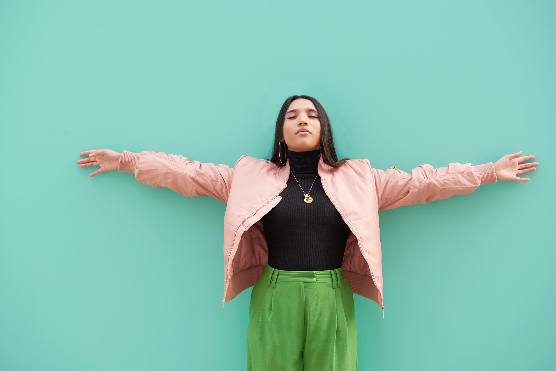 woman with arms spread and eyes closed on teal background