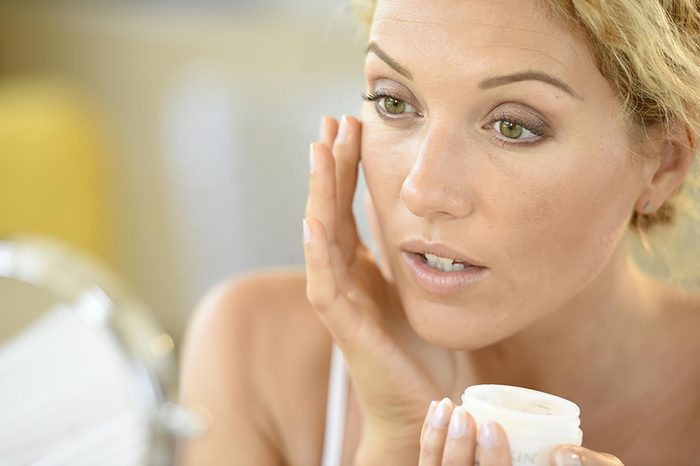 Woman applying moisturizer to her skin from a jar.
