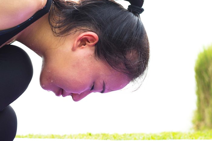 sweaty Asian woman leaning forward, eyes closed