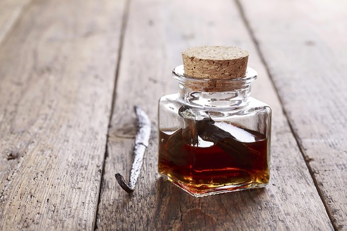 vanilla in a small corked glass jar on a wooden table next to a vanilla bean