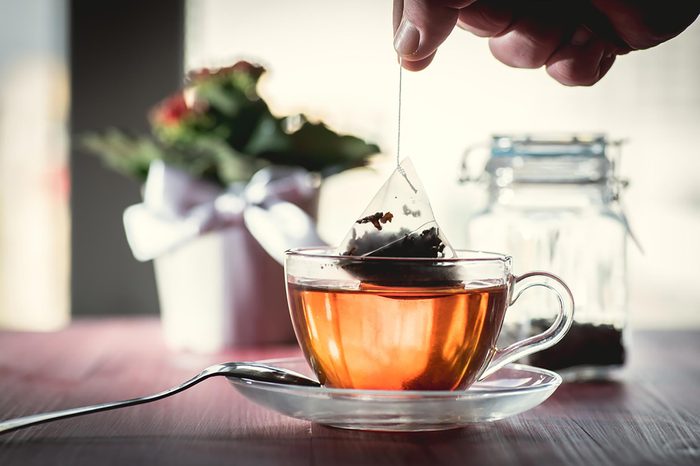 close up os a cup of tea in a clear cup with a hand holding a tea bag
