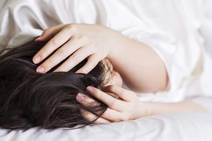 woman in bed with a headache holding her hands to her head