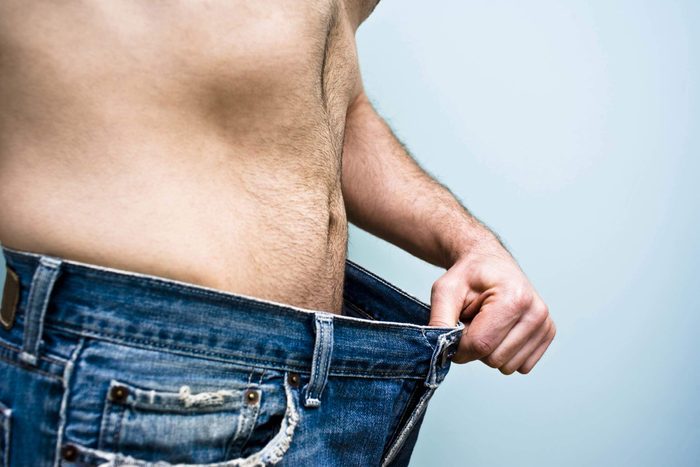Man in jeans stretching out the loose-fitting waistband with his hand..
