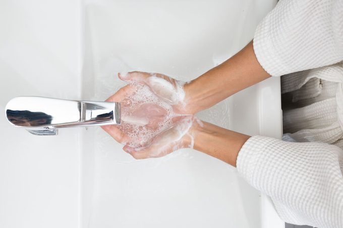 Woman in a bathrobe is washing hands.