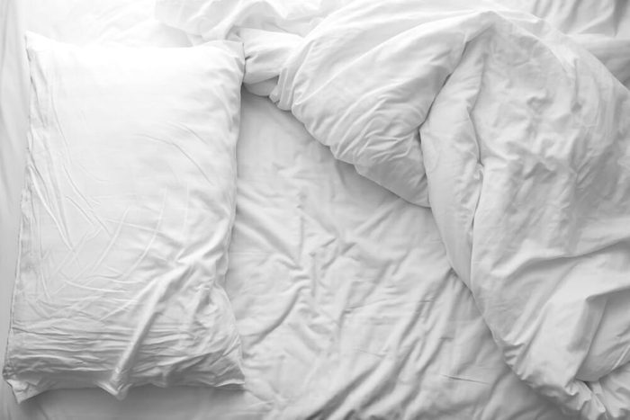 Messy bed. White pillow with blanket on bed unmade. Concept of relaxing after morning. With lighting window. Black and white theme.