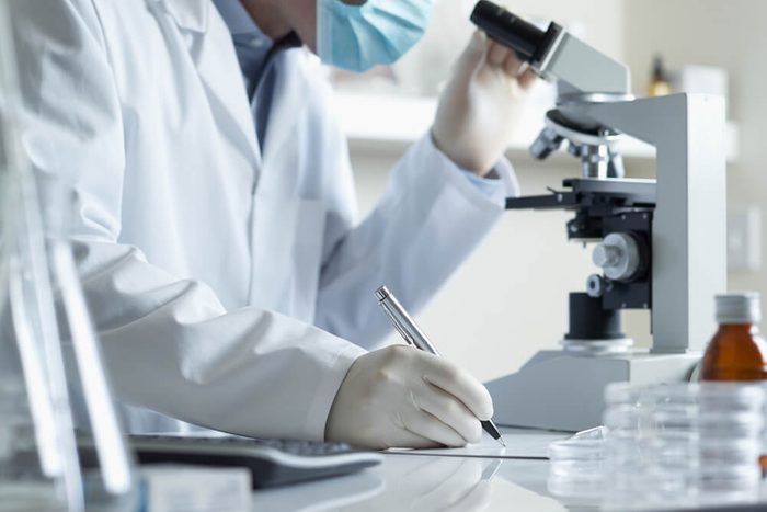 Scientist conducting research taking notes whilst looking through microscope selective focus