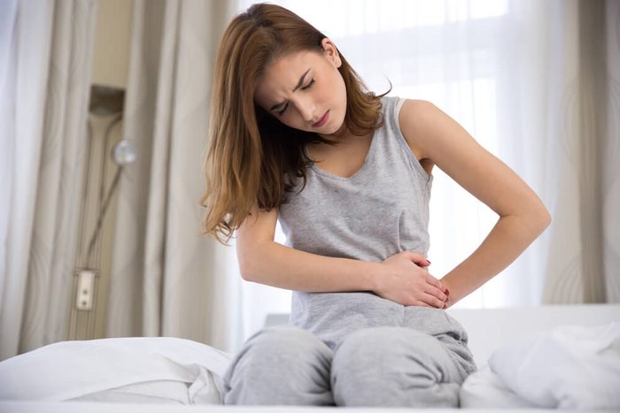 Young woman sitting on the bed with pain