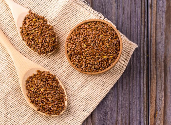 Bowl of whole flaxseeds, two wooden spoons full of flaxseeds