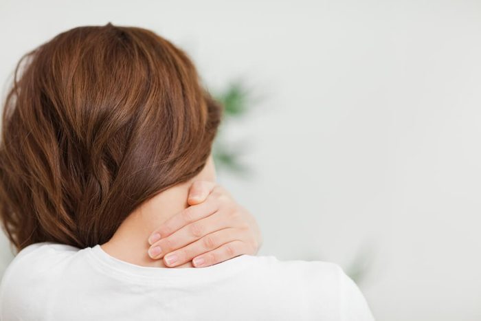 Close up of a brunette woman massing her neck in a room