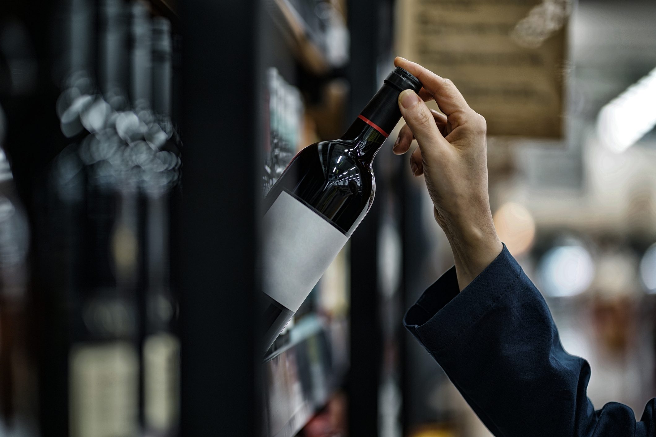 close up of woman's hand taking wine off store shelf