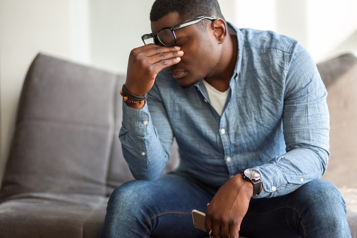 Feeling exhausted. Frustrated young black man massaging his nose and keeping eyes closed while sitting at his working place in office