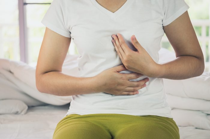woman holding center of chest and stomach while sitting on bed