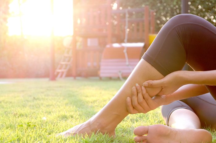 woman massaging her calf in a yard with playground