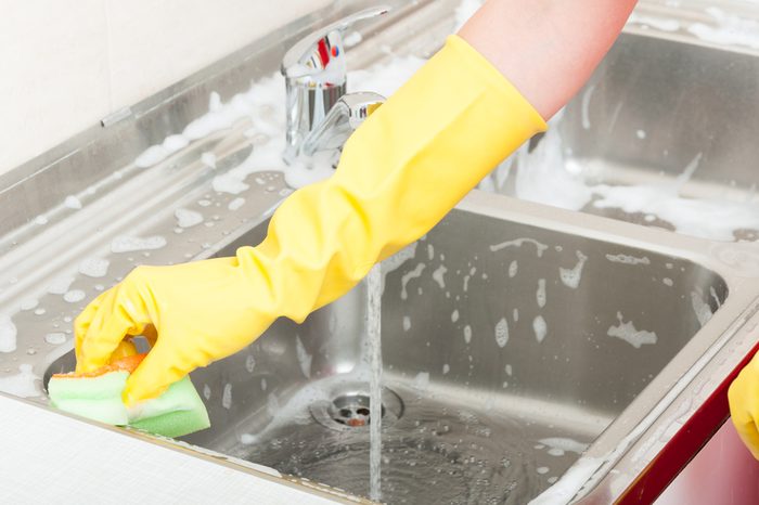 Woman cleaning sink with a sponge and rubber-gloved hand