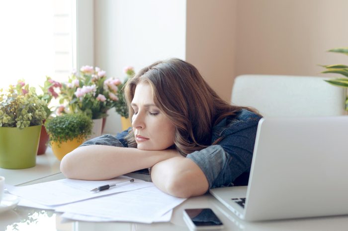 woman leaning on her desk, work in front of her, eyes closed