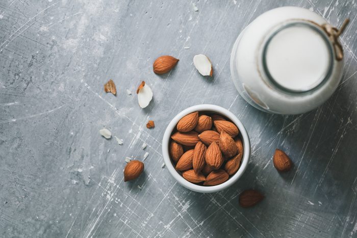 Top view of the almond milk in the glass bottle with almond nuts in the white bowl on the grey table.
