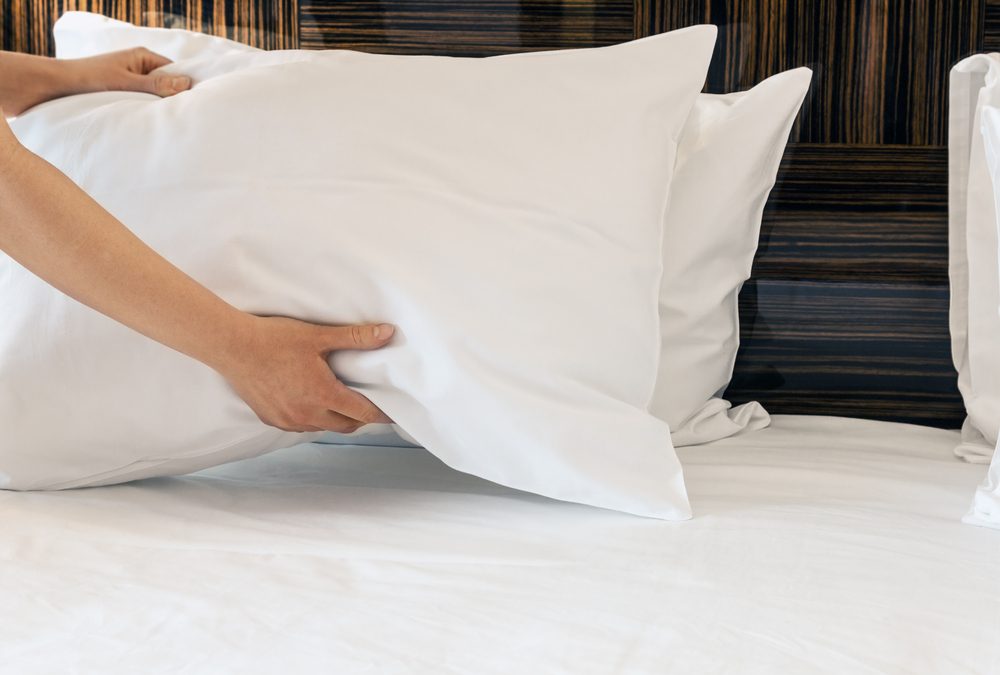 female hands corrected pillow on the bed. Concept on preparation of bed in a hotel room or at home