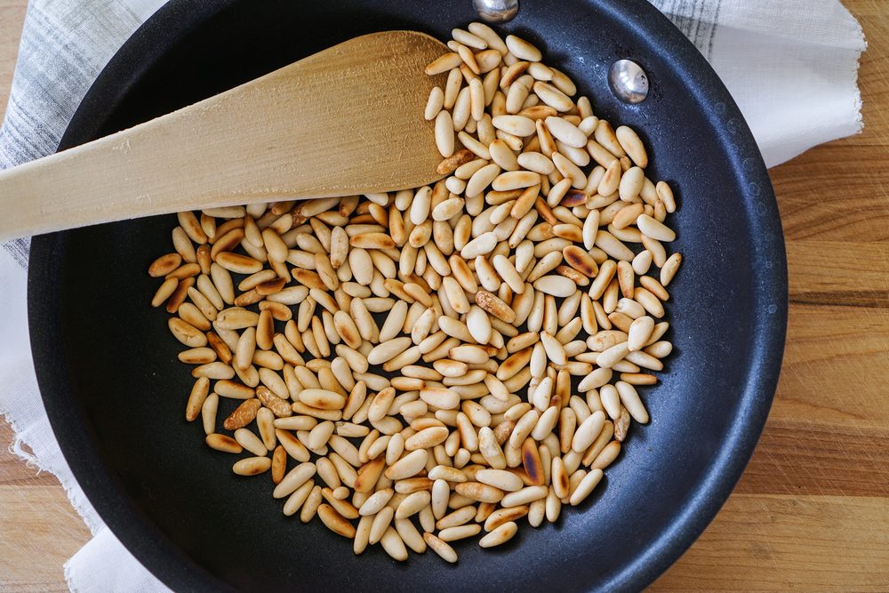 toasted pine nuts in skillet/pan on wood background