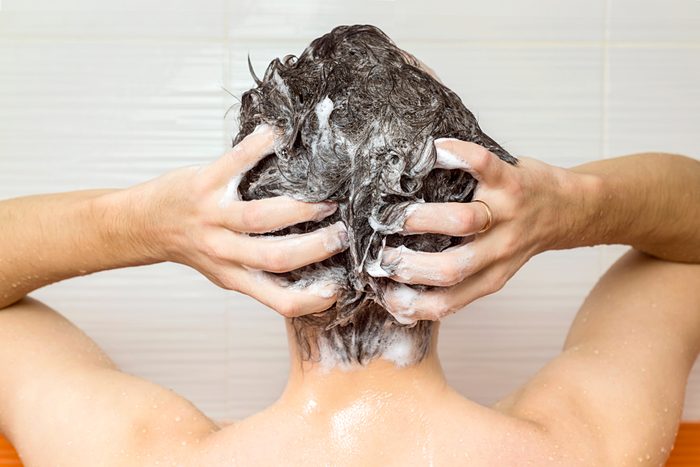 young manis washing his hair, taking a shower with foam on his head holds fingers in hair in bathroom, he use shampoo, attractive young guy is cleaning his body, health care concept