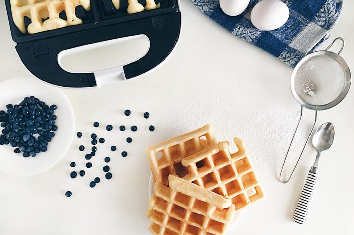 Making Belgian waffles at home - waffle iron, kitchenware and ingredients - fresh blueberry, eggs and flour.