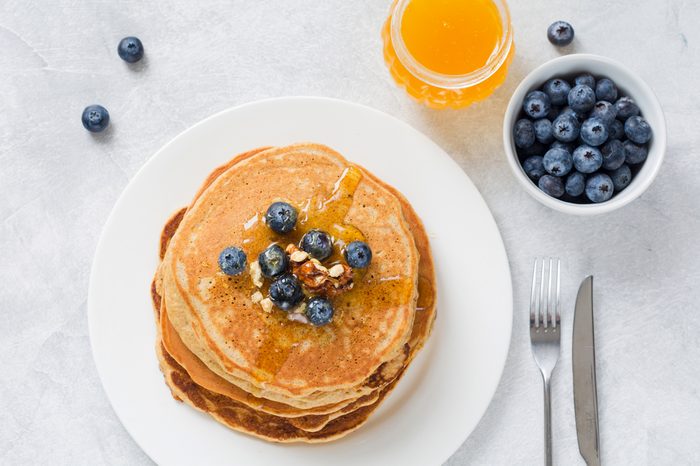 Stack of pancakes with fresh blueberries, nuts and honey on white plate.