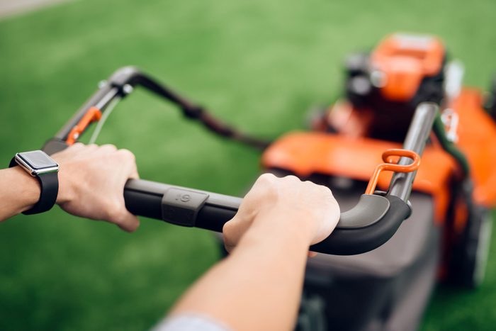 A man holds a lawn mower for the handle. He came to the tools store for gardening. He has a wristwatch on his hand.