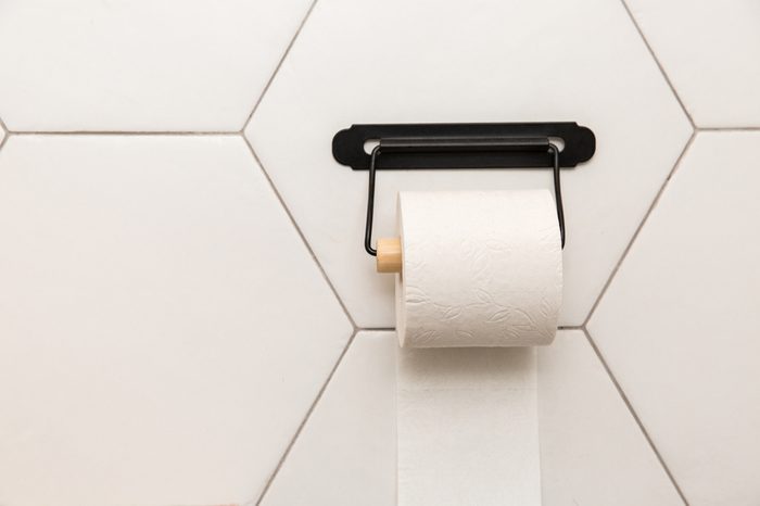A white roll of soft toilet paper hanging on a modern chrome holder on a light bathroom wall.