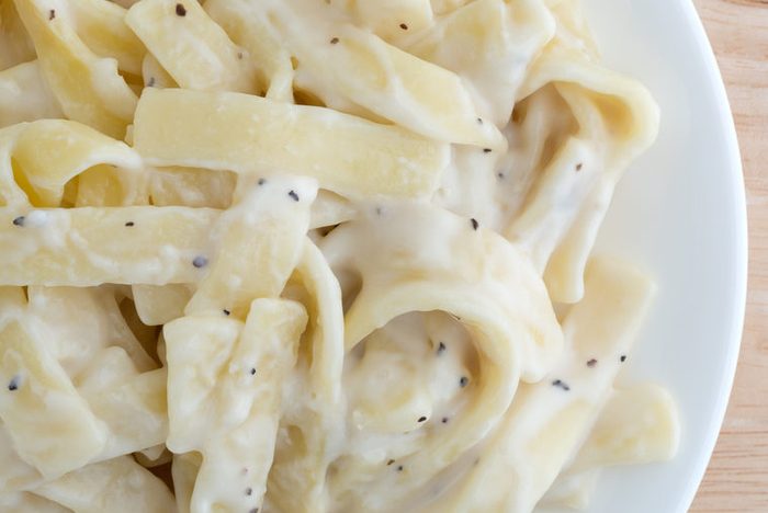 White fettuccine alfredo spaghetti on a white plate.