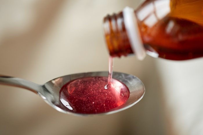 healthcare, treatment and medicine concept - bottle of medication or antipyretic syrup and spoon