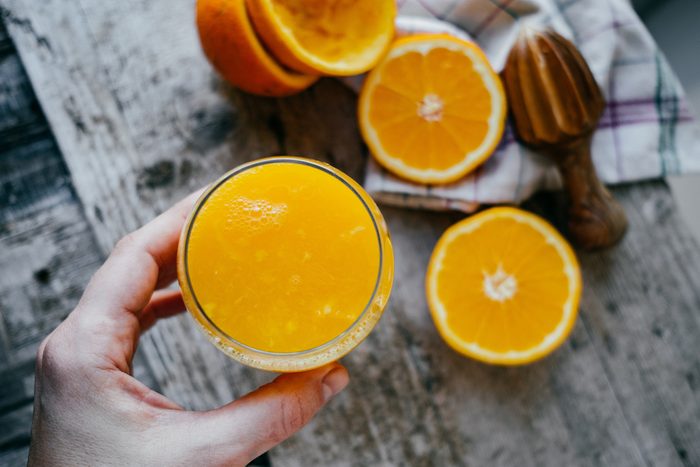 Woman's hand holding a glass of orange juice and oranges on wooden background.