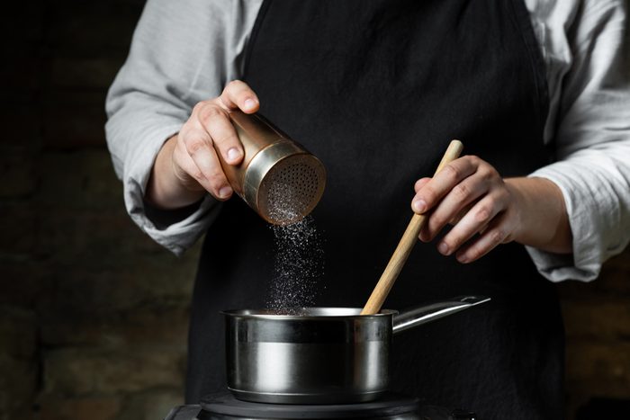 Cooking food in metal saucepan, adding salt by chef hands. Food concept background.