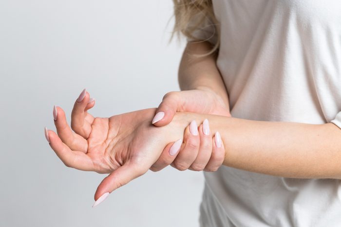 Closeup of female arms holding her painful wrist caused by prolonged work on the computer, laptop.Carpal tunnel syndrome, arthritis, neurological disease concept.Numbness of the hand
