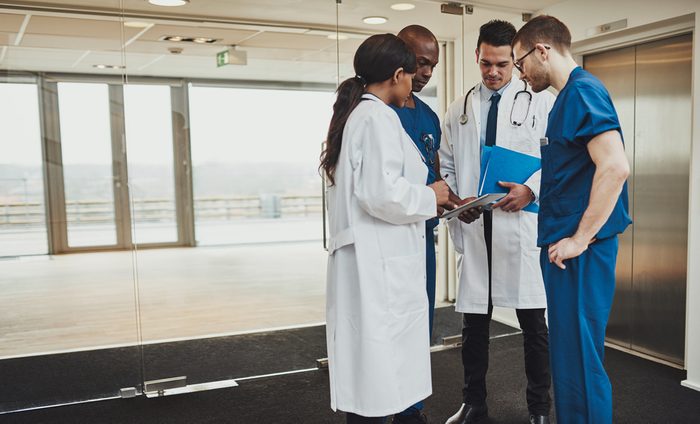 Diverse multiracial medical team consulting on a patient records standing in a foyer at a hospital grouped around a tablet computer
