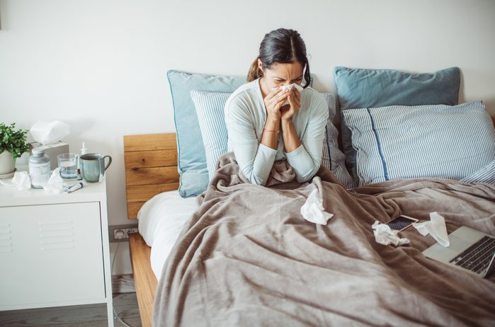 woman sitting in bed blowing nose