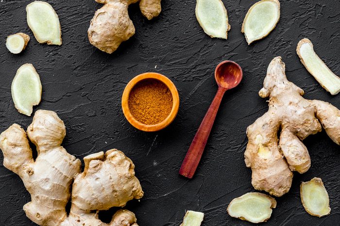 Seasoning. Ground ginger in small bowl near sliced ginger root on black background top view