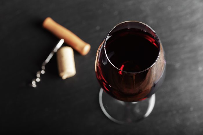 wine glass of red wine with a corkscrew. On a black wooden background.